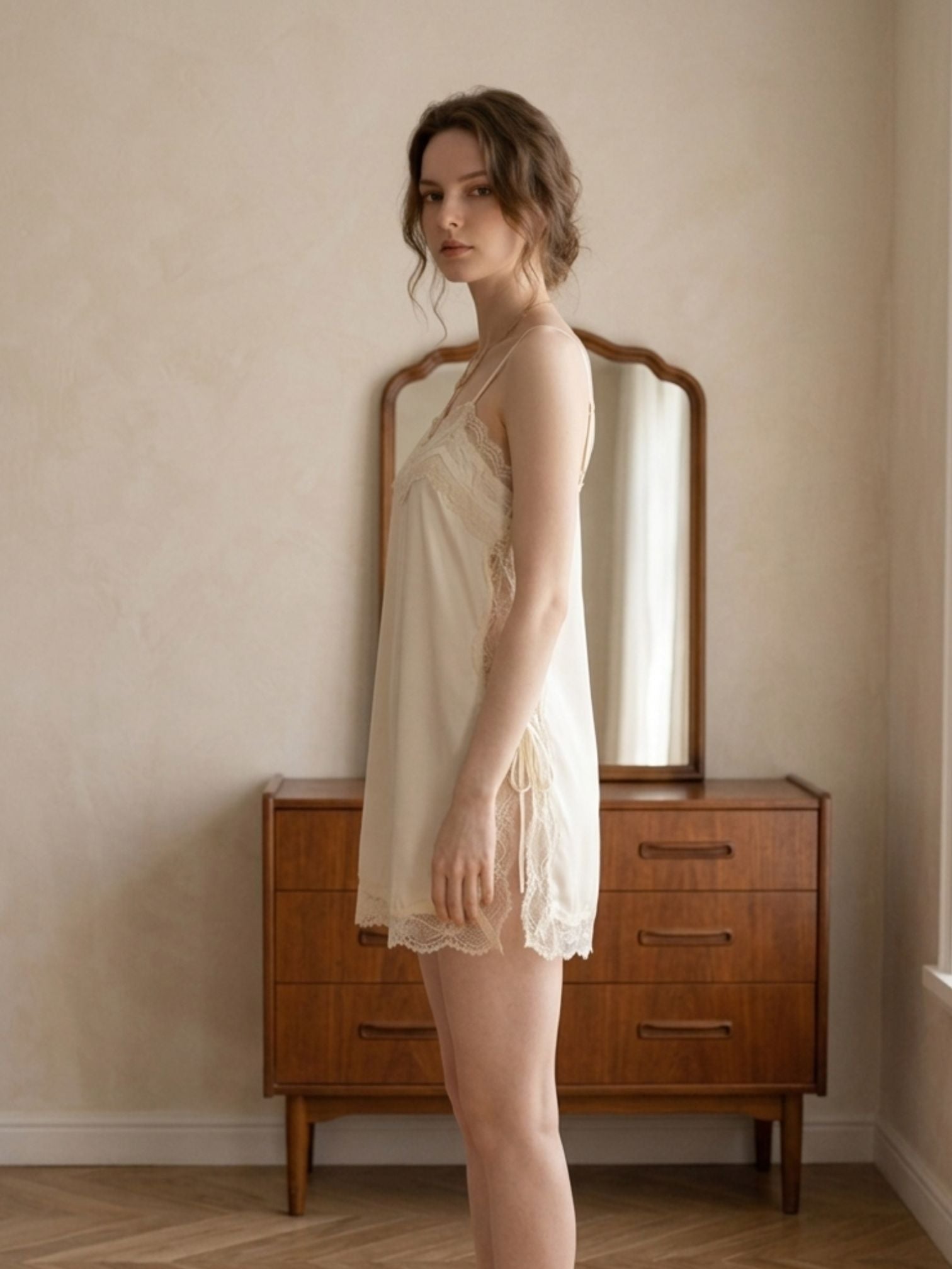 Woman in a white nightgown standing in a room with wooden furniture.