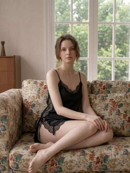 Woman in black lace lingerie sitting on a floral-patterned couch with a window in the background
