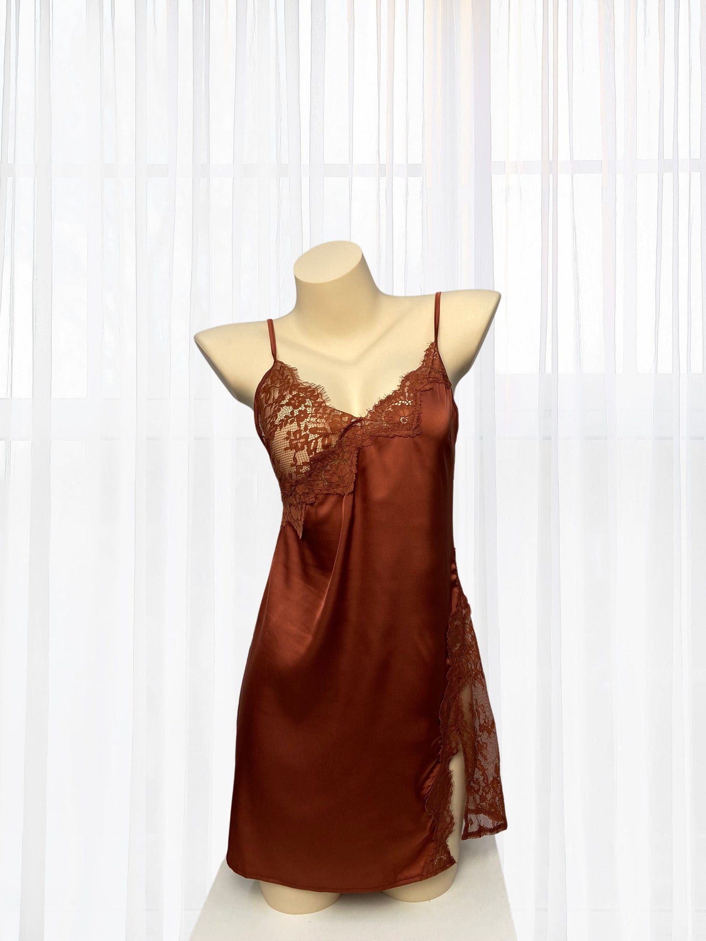 Brown satin slip dress on a mannequin against a white curtain background