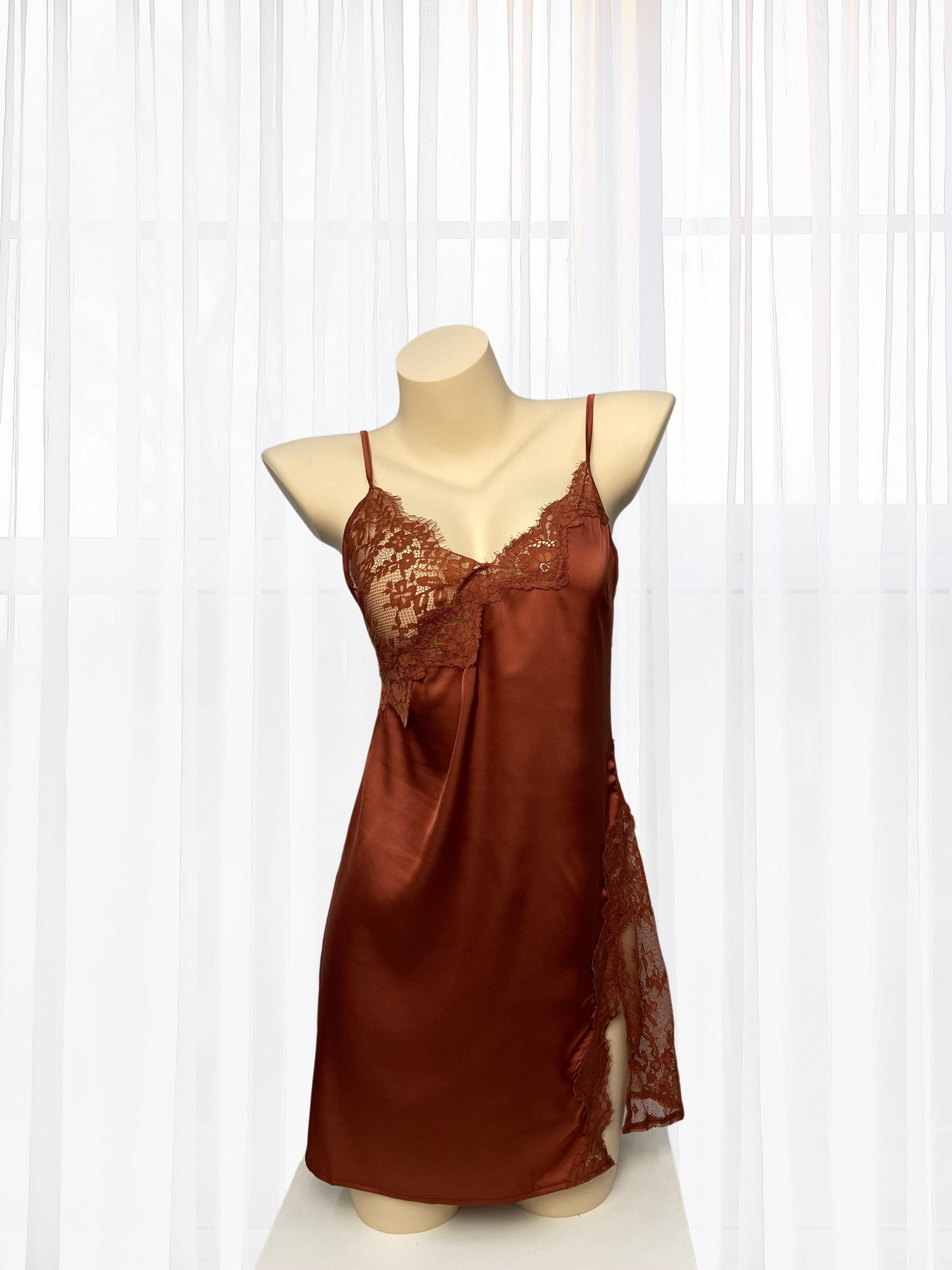 Brown satin slip dress on a mannequin against a white curtain background