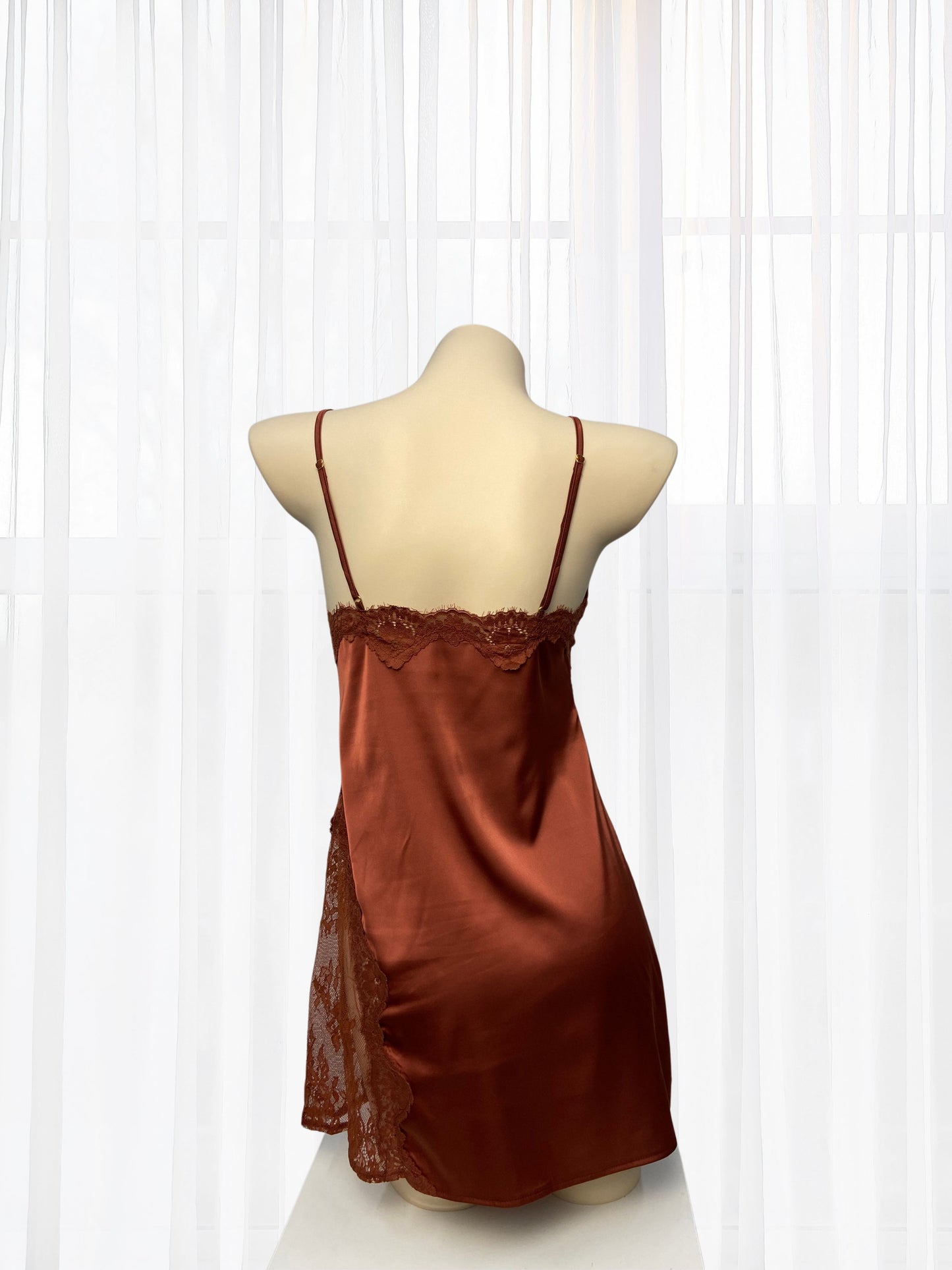 Brown satin slip dress on a mannequin against a white curtain background