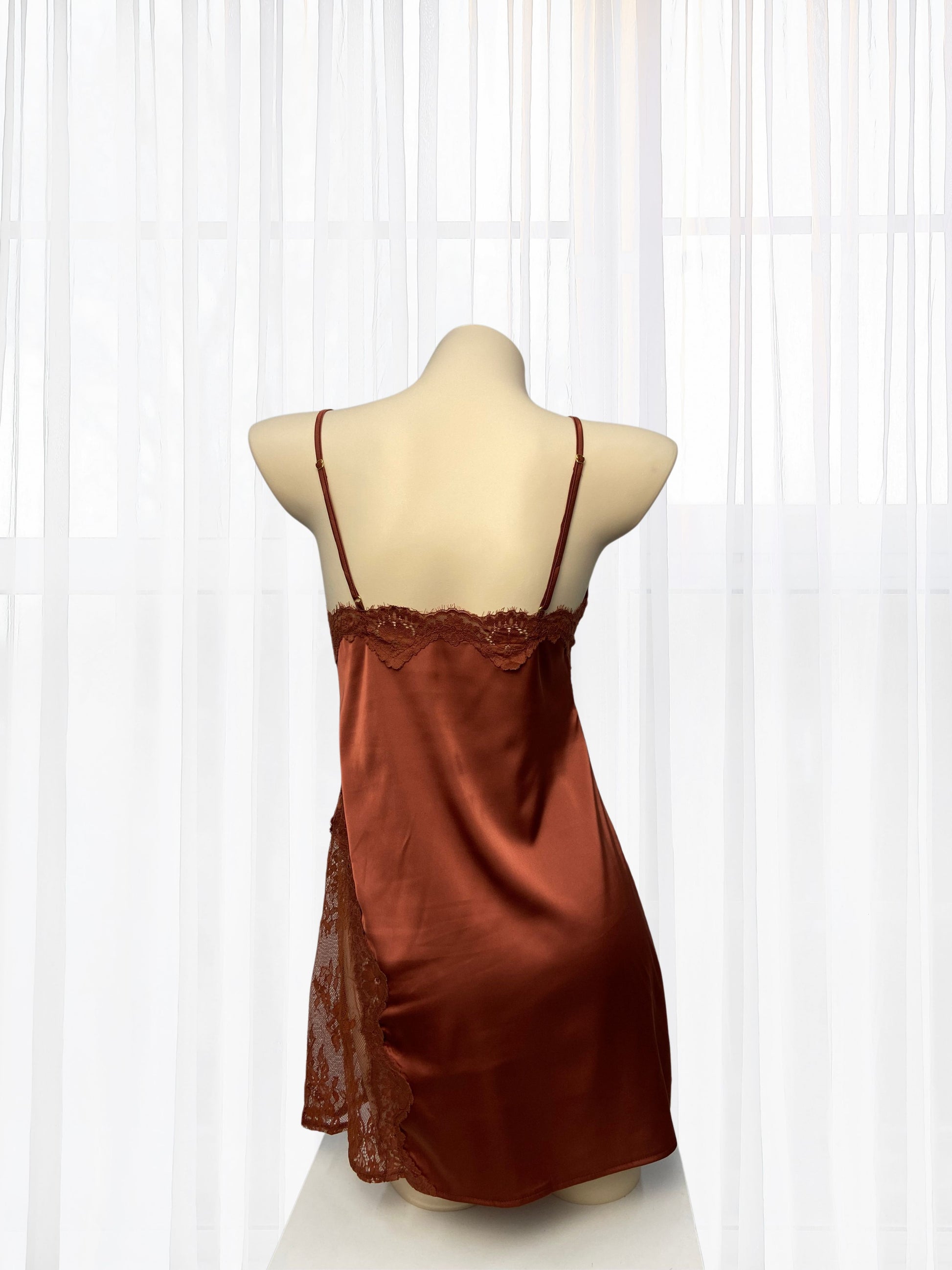 Brown satin slip dress on a mannequin against a white curtain background
